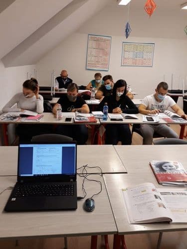 előtérben laptop, háttérben oktatók feladatot oldanak